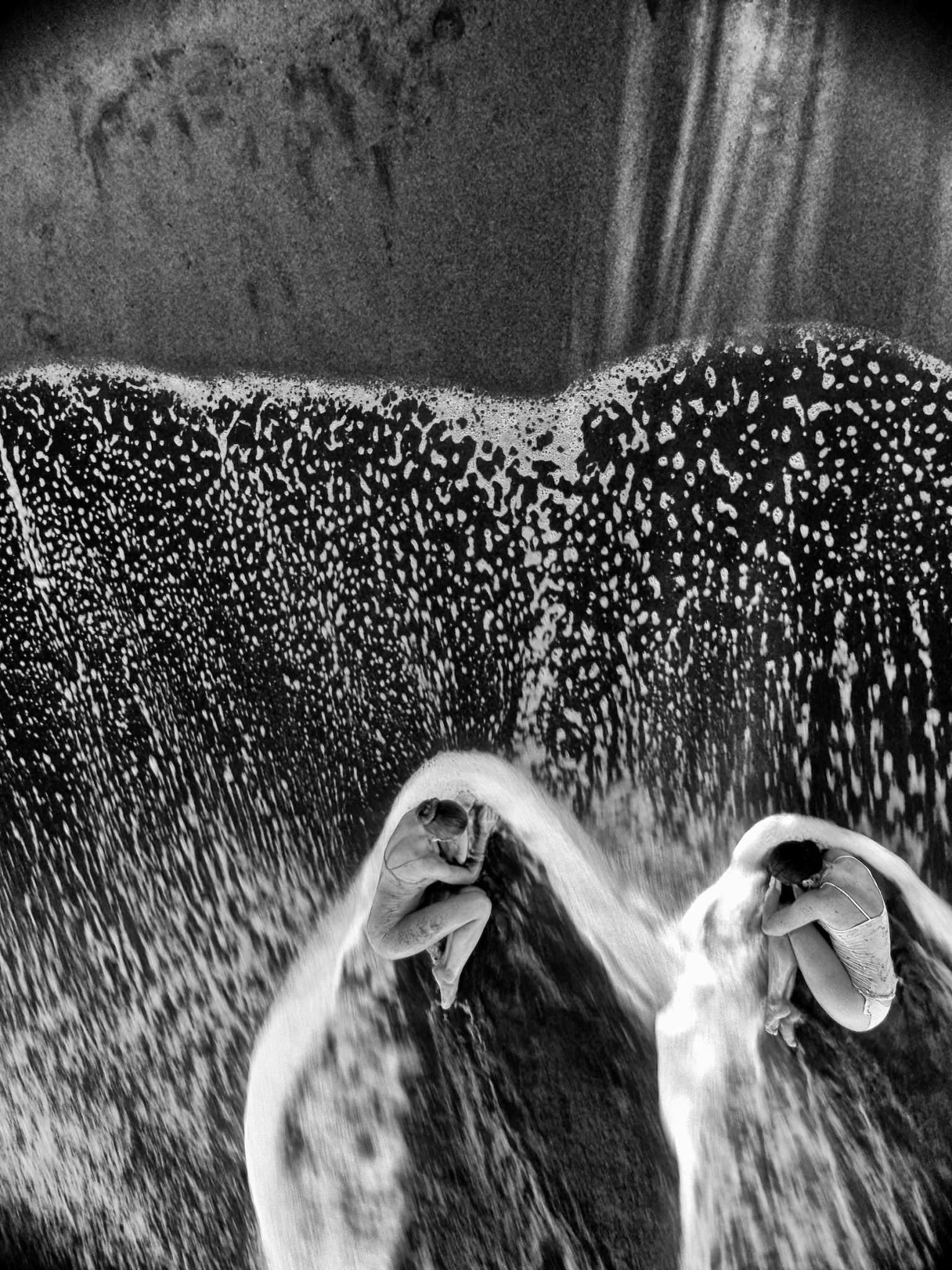 Black-and-white aerial photograph of two ballet dancers surrounded by breaking waves on a Costa Rican beach.
