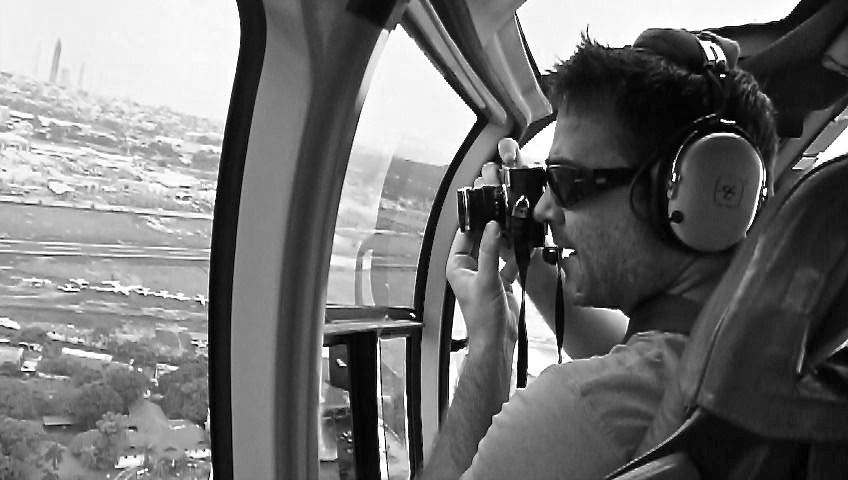 Kike Calvo photographing through a helicopter window above Panama while wearing an aviation headset.